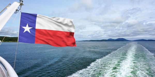 Texas flag waving on a boat over open water with islands in the distance.