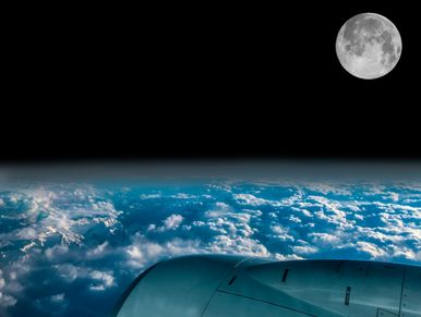 View of the moon and Earth’s clouds from an airplane window at night.
