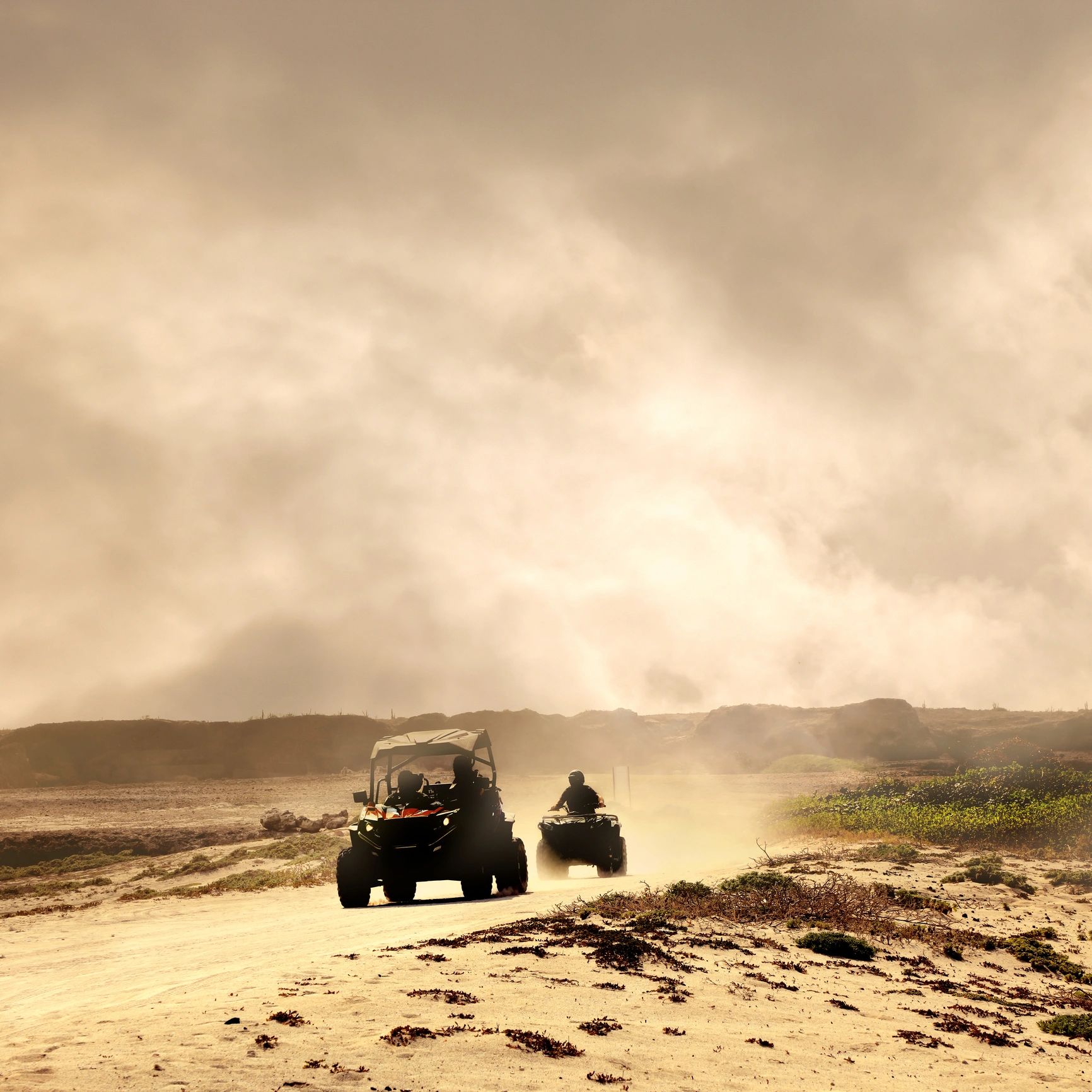 Two off-road vehicles kicking up dust on a sandy trail.