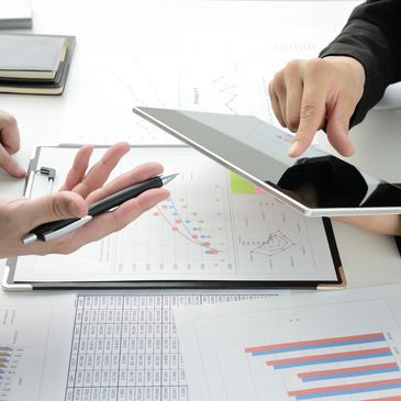 Two professionals discussing data charts using a tablet and printed reports.