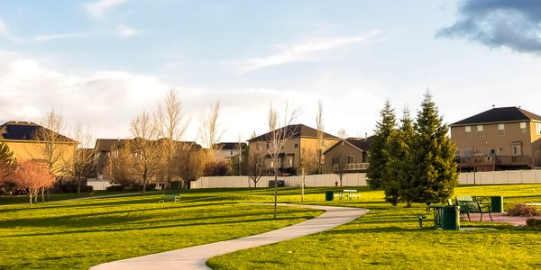 Sunlit suburban park with pathway, benches, and green lawns.