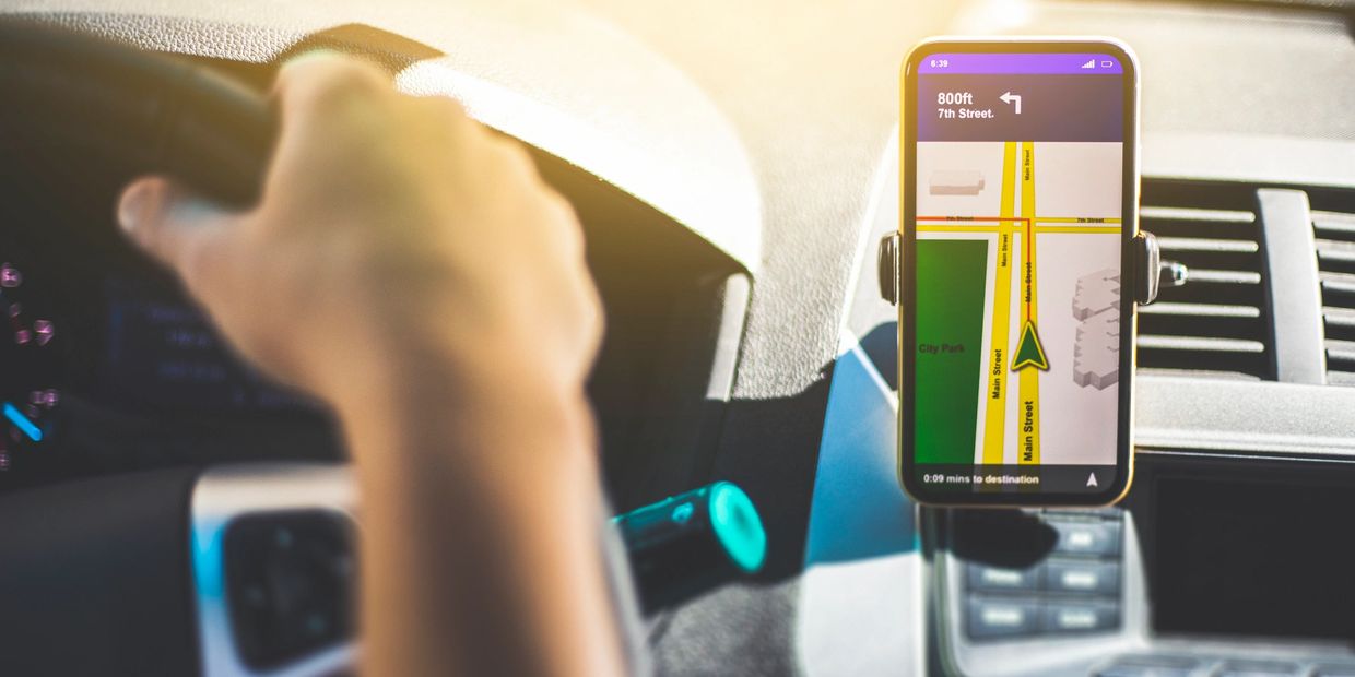 Driver holding steering wheel with GPS navigation on phone.