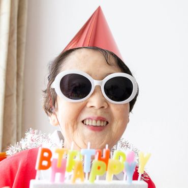 Smiling elderly woman wearing sunglasses and a party hat celebrating a birthday.