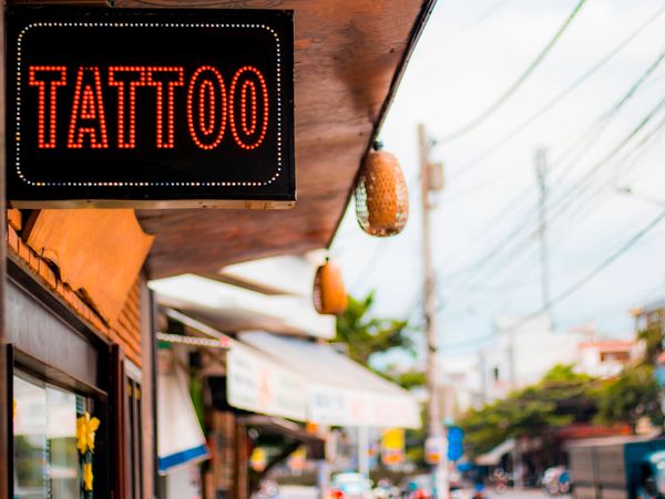 Bright neon sign reading 'TATTOO' outside a shop on a busy street.