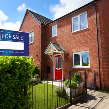 Modern brick house with red door and 'For Sale' sign in front yard.