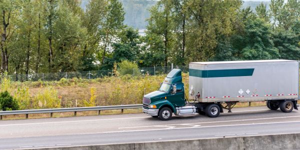 Green semi-truck driving on a highway with trees in the background.