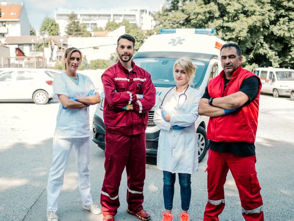 Four confident emergency medical professionals standing in front of an ambulance.