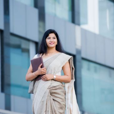 Confident woman in a sari holding a book outdoors.