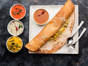South Indian masala dosa with chutneys and sambar on a white plate.