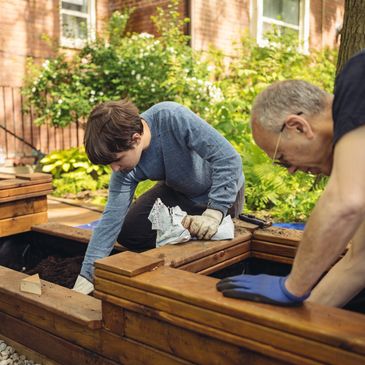 Two people working on a wooden planter box outside.