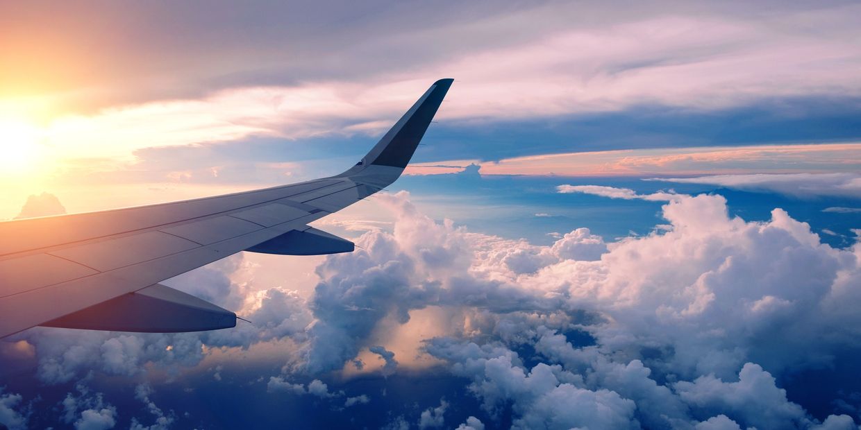 View of an airplane wing above fluffy clouds during sunset.
