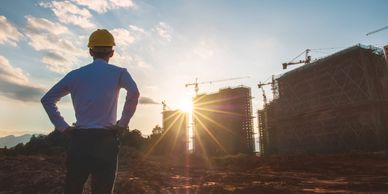 Engineer observing construction site during sunset with cranes and buildings.
