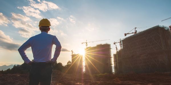 Engineer overseeing a construction site at sunset with cranes and buildings.