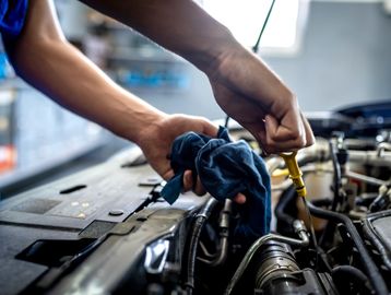 Person checking car engine oil with a dipstick and cloth.