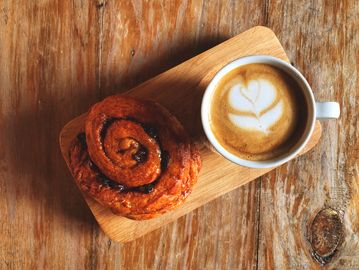 Cinnamon roll and coffee with latte art on a wooden board.