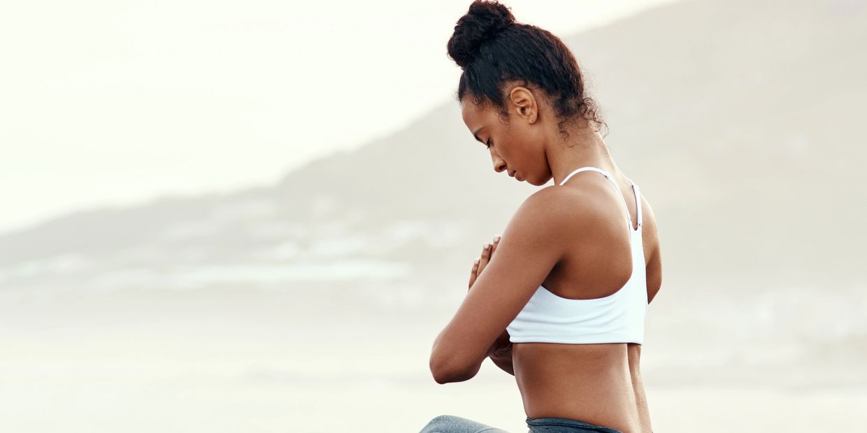 Woman meditating outdoors with mountains in the background.