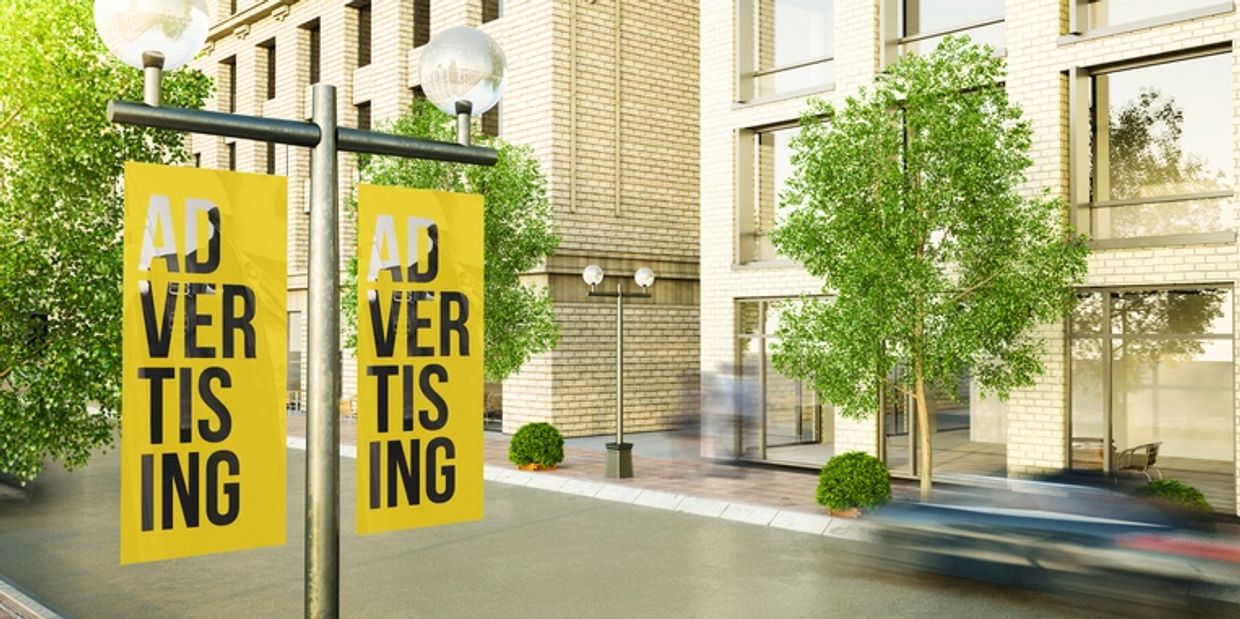Yellow advertising banners hang on poles in a sunny urban street.