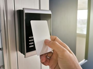 Hand holding access card near a door keypad.