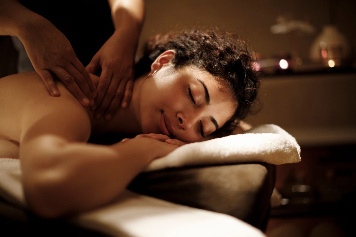 A woman enjoys a relaxing shoulder massage in a softly lit room.