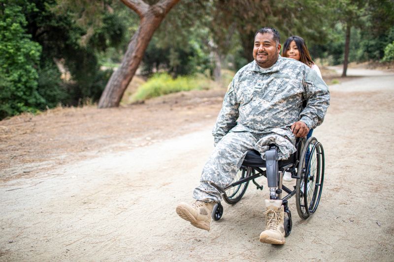 A little hispanic girl pushing her Army Veteran father in a wheelchair.