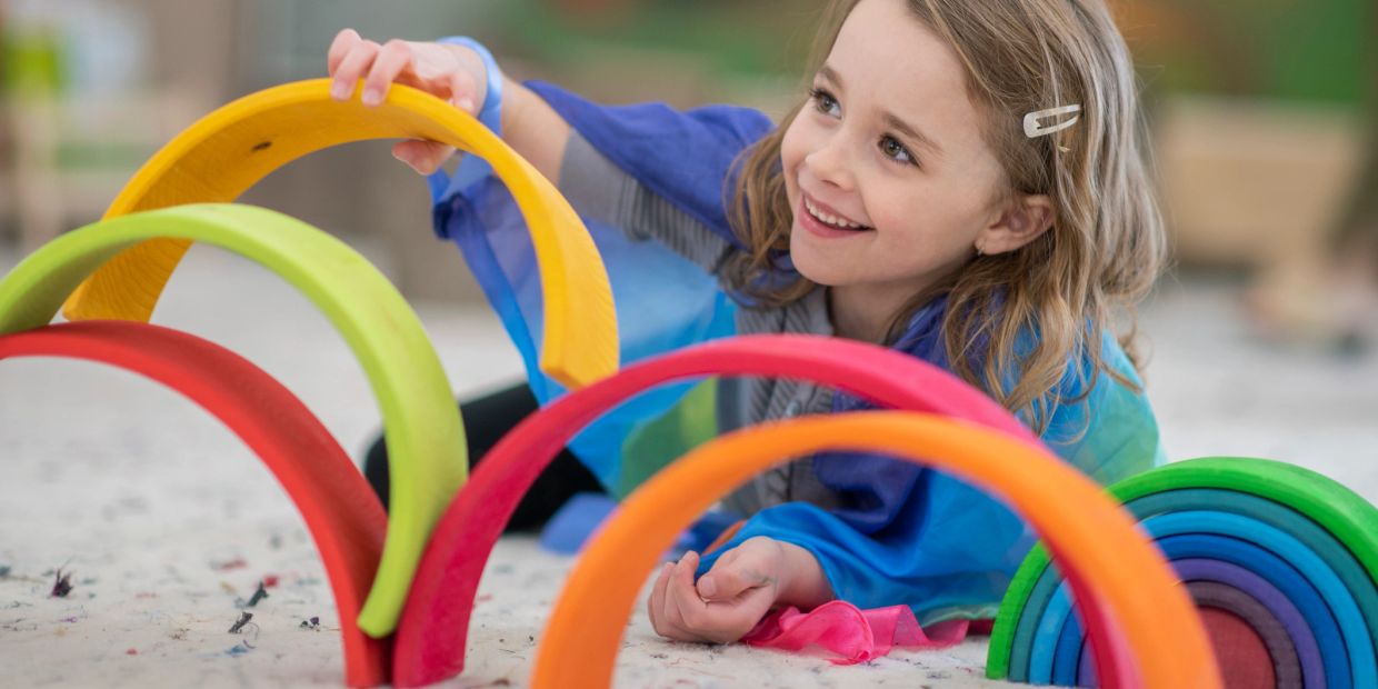 A smiling girl plays with colorful wooden arches indoors.