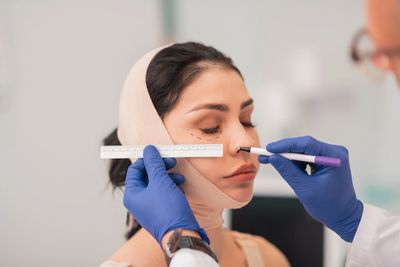 Doctor marking a woman's face for plastic surgery with a ruler and pen.