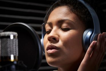 A woman wearing headphones singing passionately into a microphone in a recording studio.
