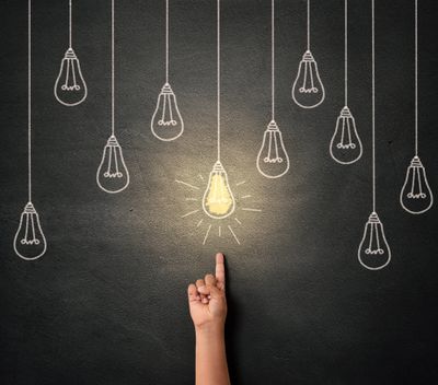 Hand pointing to a glowing light bulb drawn on a black wall.