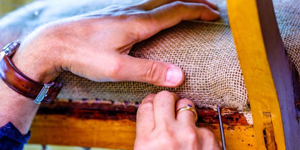 Hands upholstering a chair with burlap fabric.