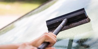 Person cleaning a windshield with a squeegee.