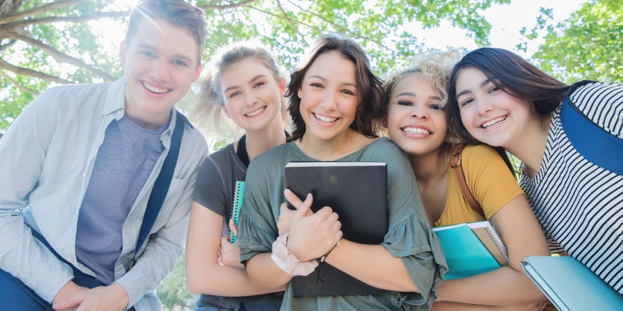 Group of five happy young students with books outdoors.