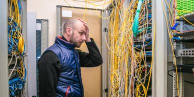 Man stressed looking at tangled network cables in a server room.