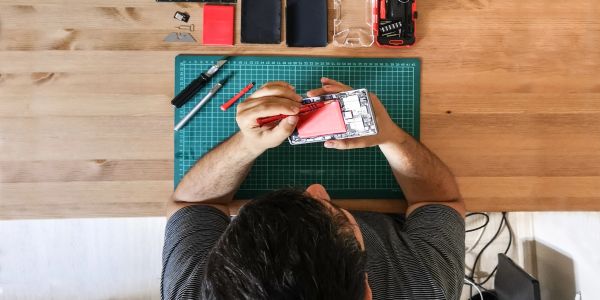 Person repairing a smartphone on a wooden table with tools.