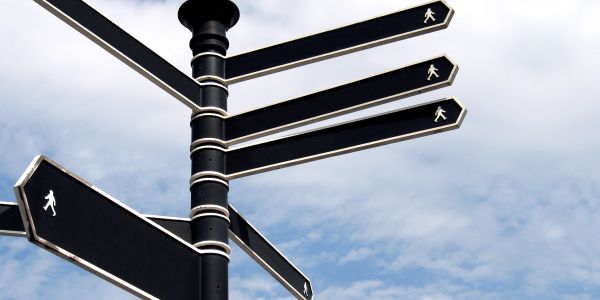 Black pedestrian direction signs against a cloudy sky.