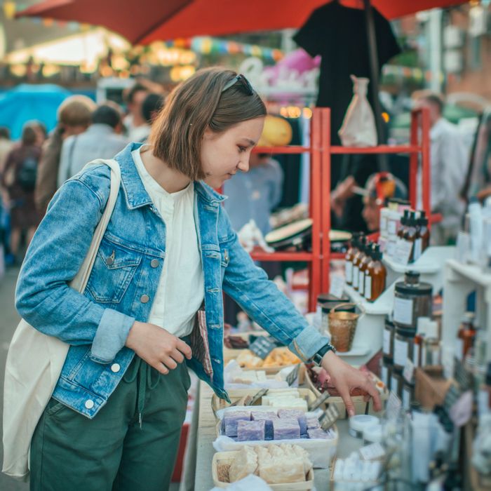 Young woman browsing artisanal soaps at an outdoor market stall.