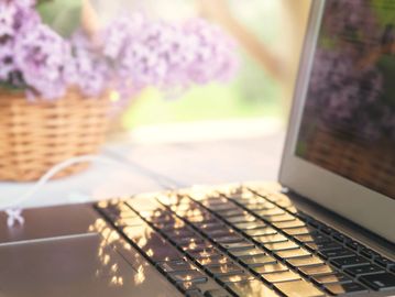 Sunlight reflecting on a laptop keyboard with a blurred flower basket in the background.