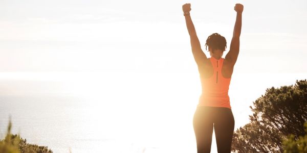 Woman raising arms in triumph at sunrise outdoors.