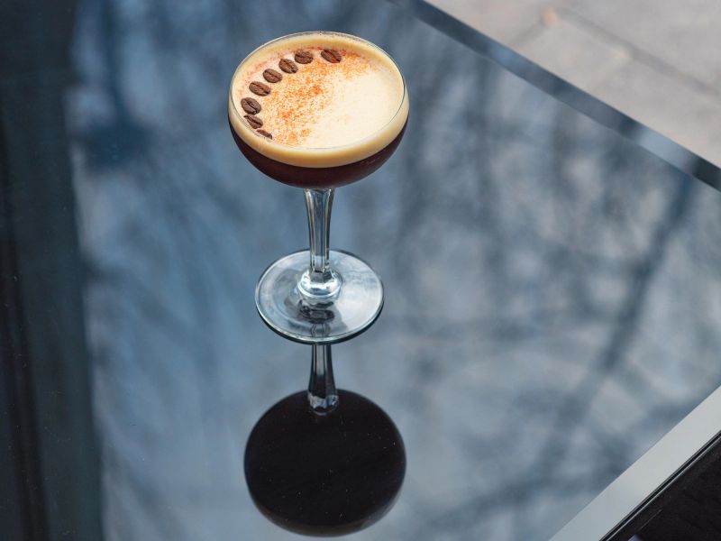 Coffee cocktail on a grey table in a transparent glass with coffee beans on top on a glass table with reflection.