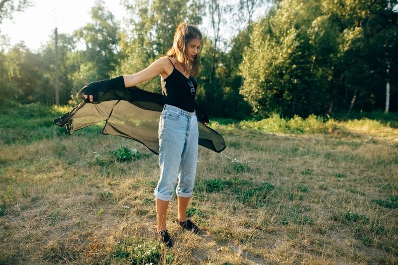 Stylish hipster girl having fun in sunny park in amazing sunbeams, atmospheric moment. Fashionable cool woman dancing and moving  in evening light. Selective focus. Retro effect. Space text