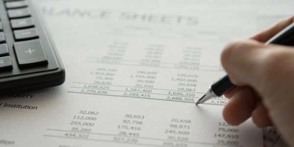 Hand holding pen over a finance sheet with calculator nearby.