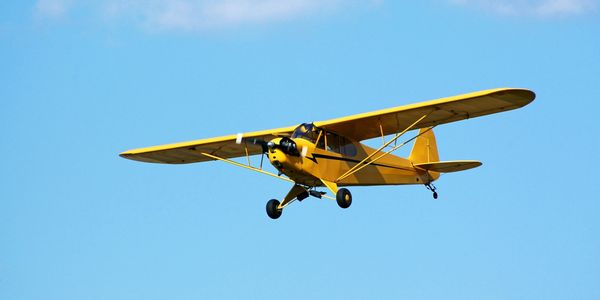 Yellow small airplane flying in clear blue sky.