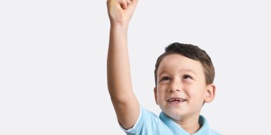 Smiling boy reaching upward with enthusiasm.