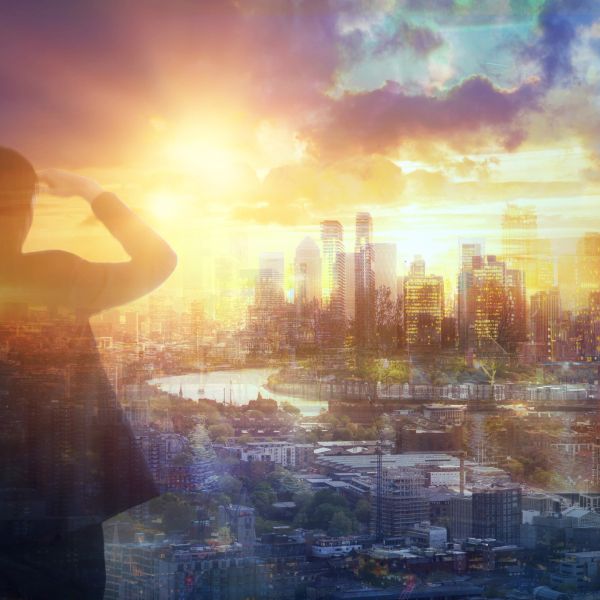 Silhouette of a person overlooking a sunlit city skyline at sunset.