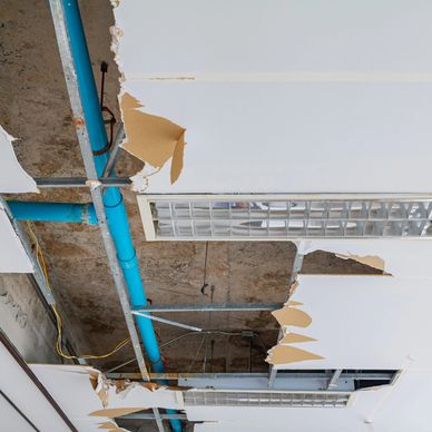 Damaged ceiling tiles exposing pipes and wiring in an office or industrial space.