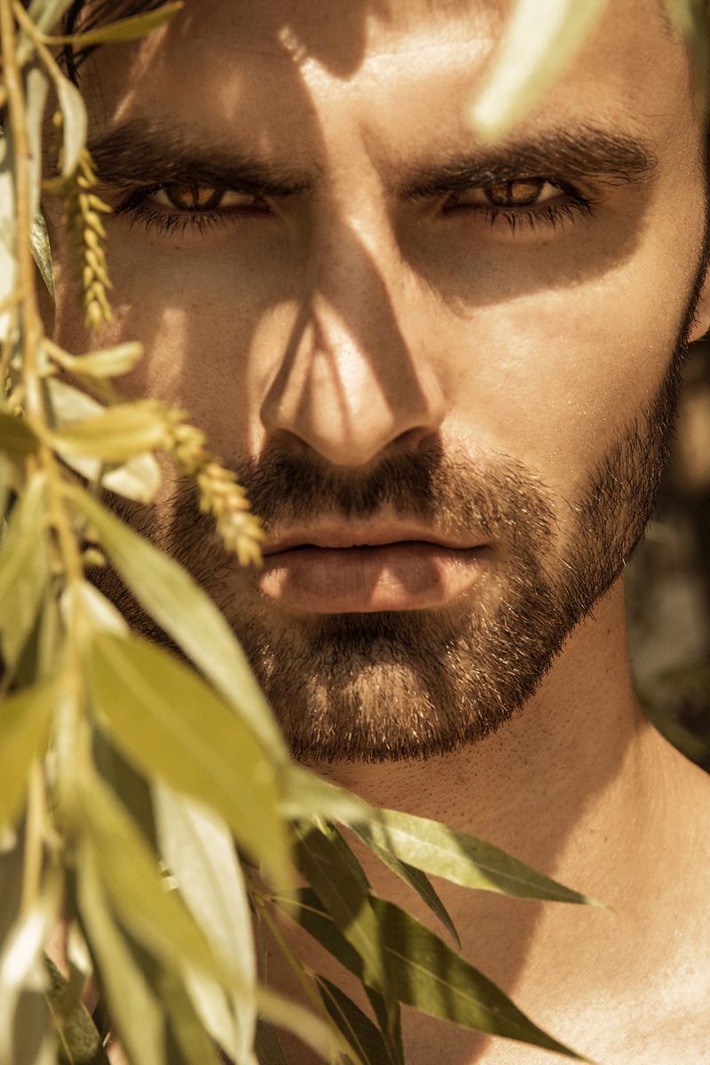 Strong face male model on the nature background with sand stones and water on the beach on the sunset