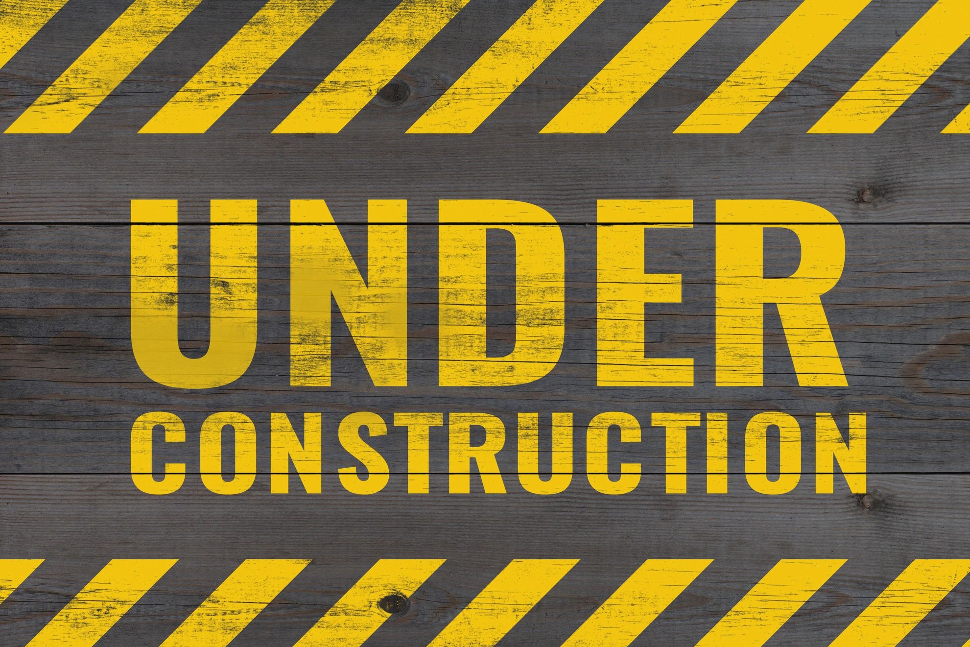 Yellow "Under Construction" sign on wooden background with caution stripes.