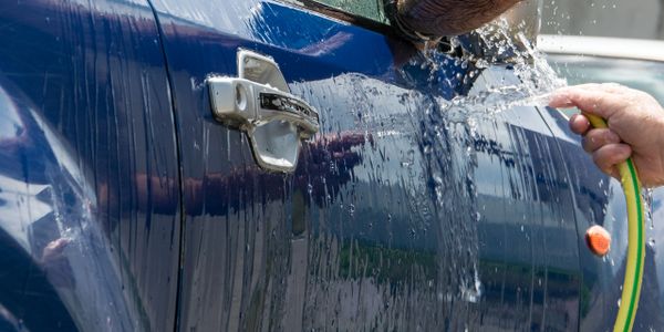 A person washing a blue car with a garden hose.