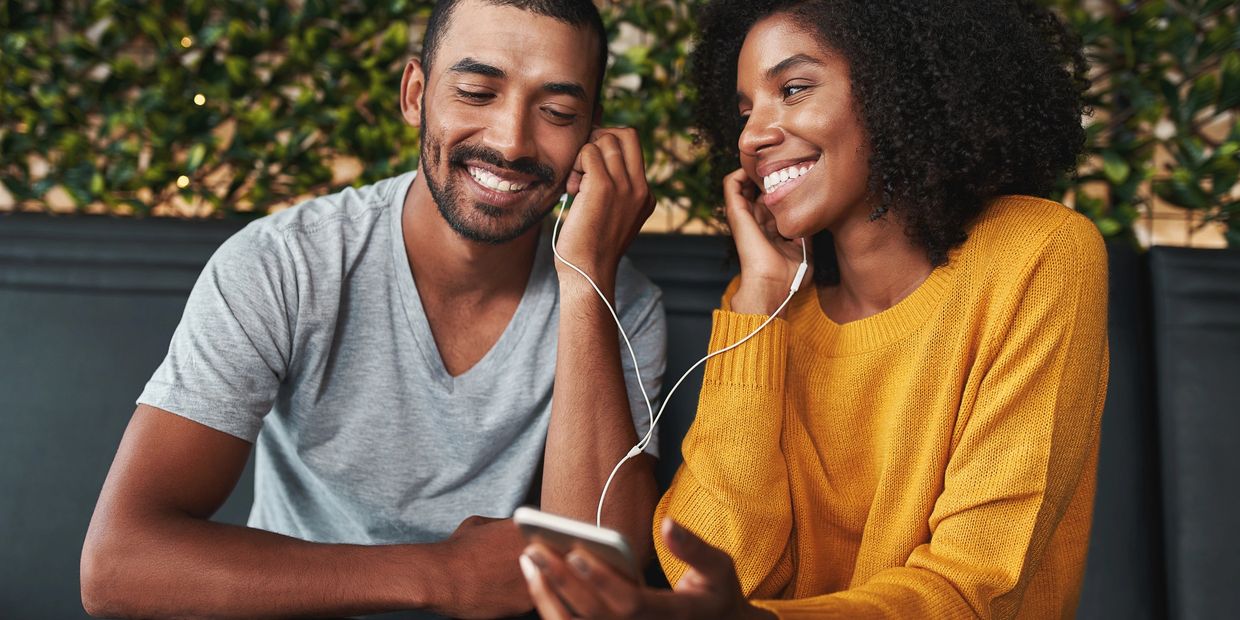 A couple sharing earphones and enjoying music together happily.