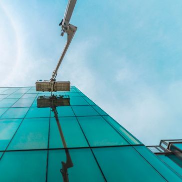 Workers clean windows on a tall glass building using a crane platform.