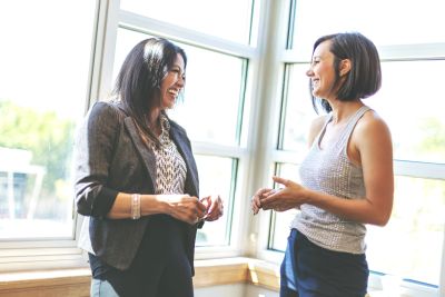 Two women smiling and chatting by a window.